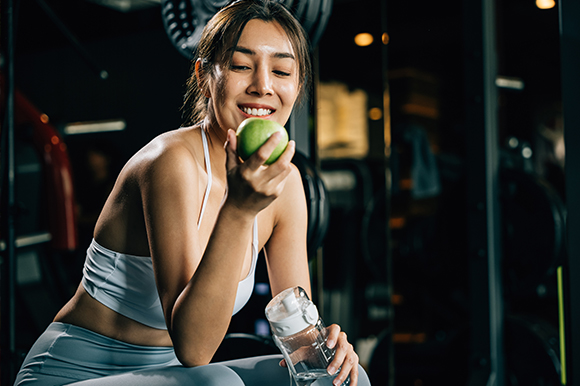 a lady holding a green apple up with one hand to eat while taking a rest from exercising