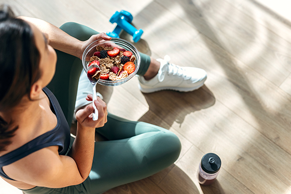a lady eating a bowl of strawberries, blackberries and bran with weights next to her