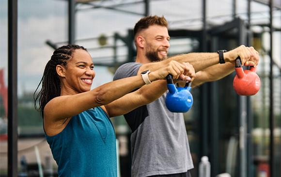 Couple lifting kettle bells at gym